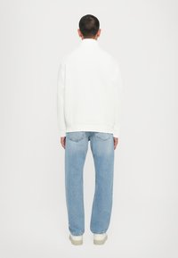 Vit sweatshirt med hög krage, som matchas med ljusblå denimjeans. Jeansen har en avslappnad passform och synlig sömnad på fickorna.