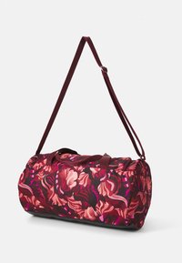 Een ronde sporttas heeft een levendig bloemenpatroon in tinten roze en bordeaux, met korte handvatten en een schouderriem.