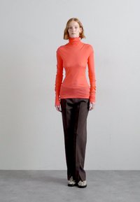 Red long-sleeve turtleneck top paired with high-waisted brown trousers and patterned shoes. Smooth fabric with a fitted design.