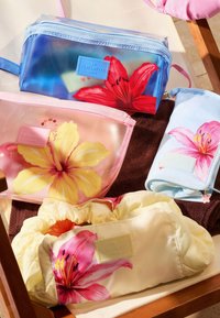Quatre pochettes de voyage à motif floral en bleu, rose, bleu clair et crème disposées sur une serviette marron sur une chaise en bois.