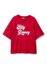 Czerwona bawełniana, oversize'owa koszulka z krótkim rękawem i okrągłym dekoltem, z białym napisem "Stay Groovy" w wyraźnej czcionce.