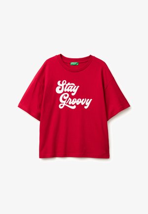 Červené bavlněné oversized tričko s krátkými rukávy a kulatým výstřihem, které má bílé texty "Stay Groovy" v tučném písmu.