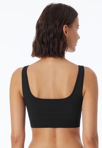 Bralette in tessuto elasticizzato nero con spalline larghe e design a schiena quadrata. Tessuto liscio senza hardware o motivi aggiuntivi.