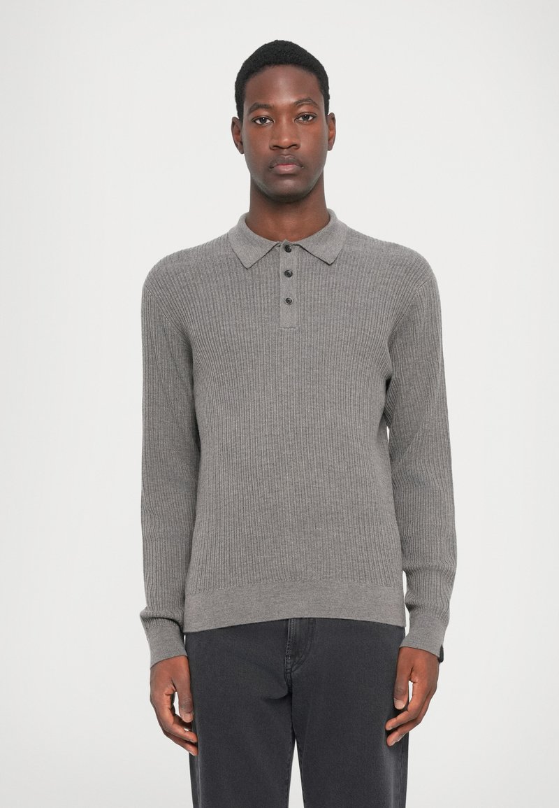 Grijs gebreid poloshirt met lange mouwen en een ribbelstructuur, sluiting met vijf knopen en platte kraag, gecombineerd met donkere jeans.