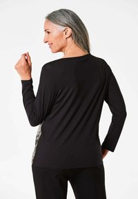 Zwarte langemouwen top met ronde halslijn, voorzien van een gestructureerd stoffenpaneel aan de zijkanten, een gladde textuur en een ontspannen pasvorm.