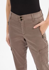 Pantalons cargo marron en tissu coton lisse, avec deux poches avant, une poche zippée sur le côté, une fermeture à double bouton et des détails de couture subtils.