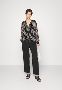 Blusa preta estampada com flores, mangas longas, decote em V, padrões de flores multicoloridos, combinada com calças largas pretas e sandálias de salto pretas.