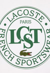 Tela blanca con un gran logotipo circular en verde. El texto incluye "LACOSTE", "PARIS" y "ROPA DEPORTIVA FRANCESA", con un cocodrilo bordado en verde.