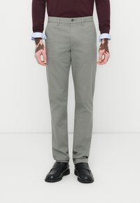 Lichtgrijze broek met een slim fit, voorzien van een knoopsluiting en zijzakken, gecombineerd met zwarte schoenen en een donker lange mouw top.