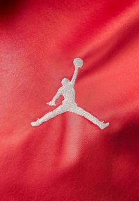 Punainen kangas, jossa on valkoinen ommeltu Jumpman-logo. Logossa on ilmassa oleva hahmo, joka pitää koripalloa, korostaen urheilullista liikettä.