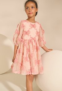 Vestido rosa bordado con flores, mangas abullonadas transparentes, tejido texturizado y falda acampanada. Acentuado con sutiles destellos por todo el vestido.