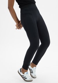 Zwarte sportleggings met een hoge tailleband, naadloos ontwerp en aansluitende pasvorm. Gecombineerd met wit- en zwartkleurige sneakers met grijze accenten.