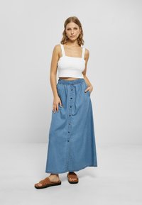 Jeans maxi skjørt har knappefront, elastisk midje og sidelommer. Kombinert med en hvit kort tank topp og brune sandaler med glidelås.