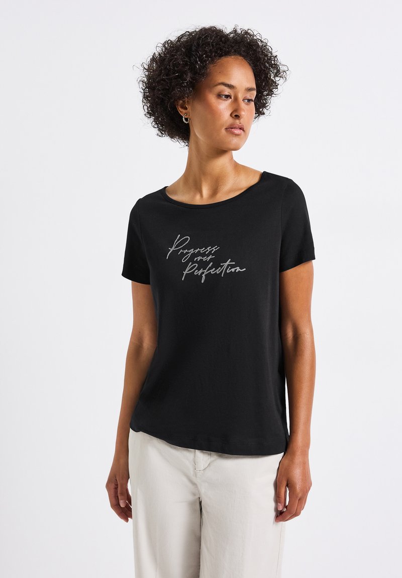 Mustapaita, jossa on lyhyet hihat ja pehmeä kangas, pyöreä pääntie ja hopeinen kirjoitus, jossa lukee "Eteneminen, ei täydellisyys."