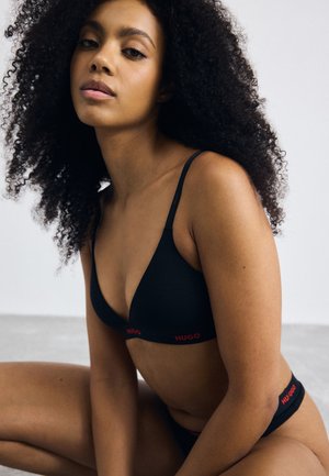 Zwart lingerieset met een triangle beha en bijpassende slip, beide met rode "HUGO" logo, zachte textuur en verstelbare banden.