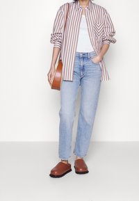 Pruhovaná košile na knoflíky v hnědé a bílé barvě, světle modré džíny rovného střihu, hnědé dřeváky a hnědá crossbody kabelka.