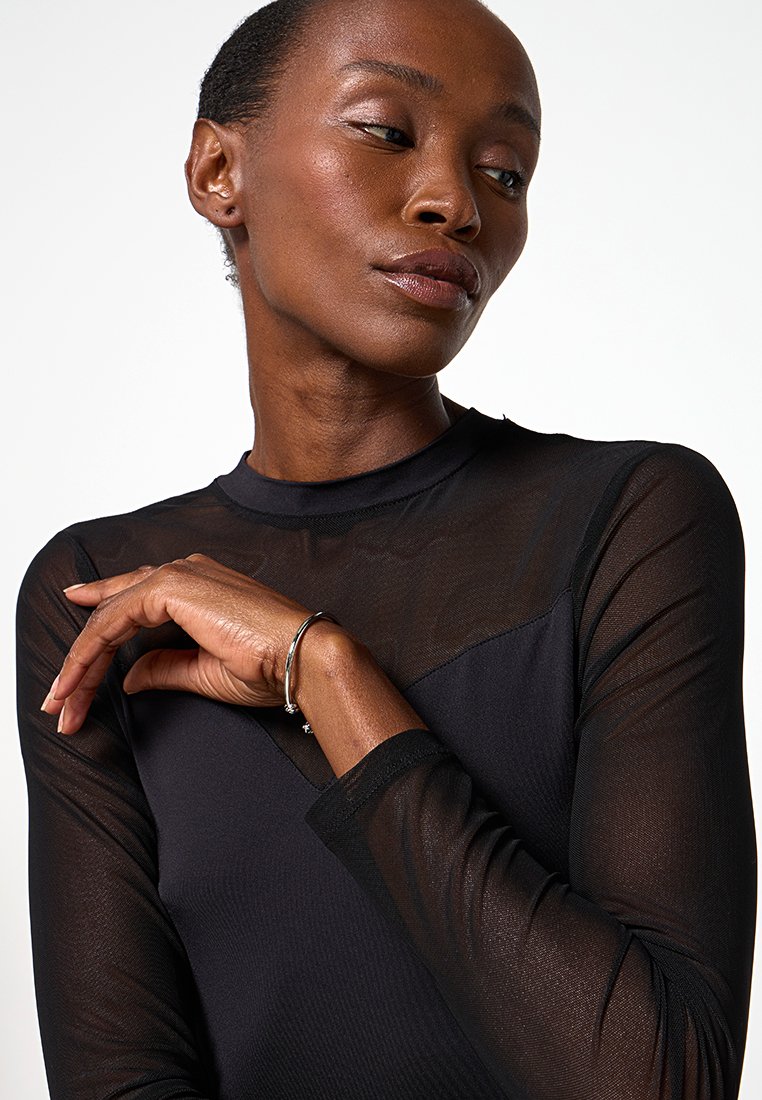 Top lungo trasparente nero a maniche lunghe con tessuto testurizzato, collo alto e un pannello solido a contrasto sul petto. Accessoriato con un bracciale.