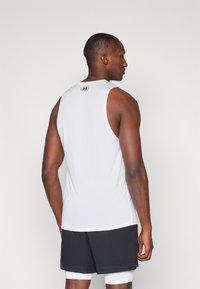 T-shirt de sport sans manches blanc en tissu respirant, avec un col rond et un subtil logo au dos. Short noir.
