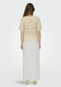 Top de croch�é beige con mangas cortas, combinado con una falda maxi blanca y fluida; los patrones texturizados y el ajuste holgado son características notables.