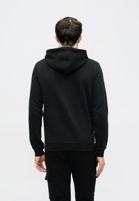 Zwarte capuchontrui met een gladde textuur, lange mouwen en een ontspannen pasvorm. Van achteren getoond tegen een effen achtergrond.