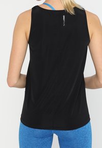 Czarny sportowy tank top o luźnym kroju, z subtelnym logo z tyłu, uzupełniony niebieskimi sportowymi spodenkami. Gładka tekstura materiału.