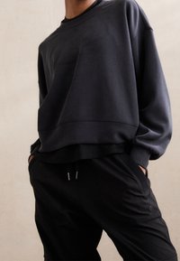 Sudadera de gran tamaño en gris oscuro con hombros caídos, tejido texturizado y dobladillo acanalado, combinada con pantalones negros de corte relajado con bolsillos.