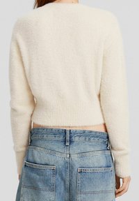 Cropped, cream sweater made of soft, fuzzy material. Features long sleeves and ribbed hem. Paired with high-waisted, light blue denim jeans.