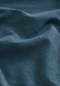 Mörk teal tyg med en mjuk och slät yta, med subtila vågor och veck som indikerar flexibilitet och smidighet.