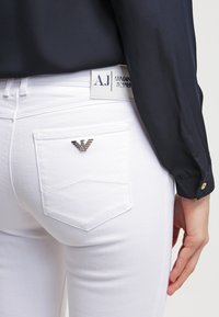 Vita jeans har en liten silverlogga på höger bakficka, med en rak passform och subtila sömdetaljer.
