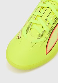 Fluorescerende gule sportssko med tekstureret overflade, der har sorte og pink accenter, spids tå og centralt snøresystem.