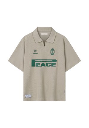 Bež kratka srajca s kratkimi rokavi z zelenim napisom "PEACE", majhno zastavo nad levim prsnem delom in ovratnikom z režo spredaj.