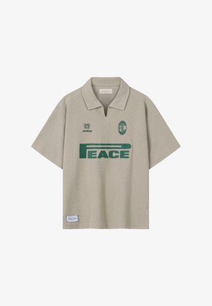 Polo beige à manches courtes avec texte vert "PEACE", petit logo au-dessus de la poitrine gauche, et col avec encoche à l'avant.
