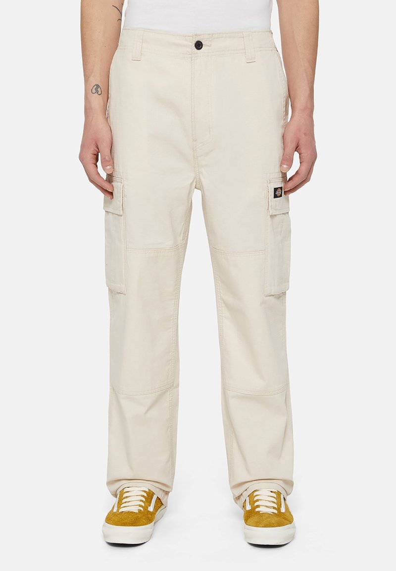 Beige cargo kalhoty se rovný fit, s bočními kapsami, poutky na pásek a decentní texturou. V kombinaci se žluto-bílými teniskami.