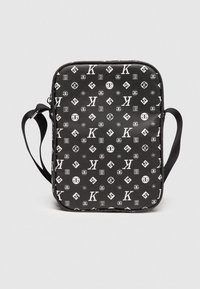 Zwarte rechthoekige tas gemaakt van textuurmateriaal, met een patroon van witte logo's en symbolen. Inclusief een lange schouderband.