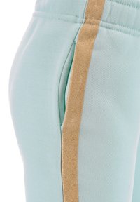 Helle blaue Jogginghose mit einer weichen Textur, ausgestattet mit einem glänzenden goldenen Streifen, der die Seite entlang verläuft, und einer Seitentasche an der Hüfte.