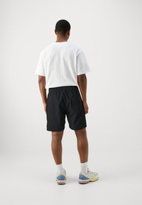 Zwarte shorts met een elastische tailleband, voorzien van een achterzak. Gecombineerd met een eenvoudig wit T-shirt en lichtgekleurde sneakers.