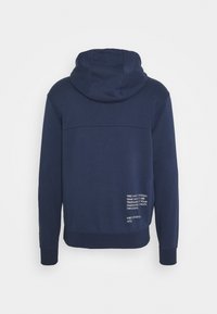 Mörkblå huvtröja med mudd på ärmslut och fåll. Har en söm baktill och vitt textmärke på nedre högra sidan.