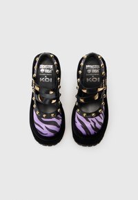 Čierne a fialové platformové topánky so zebra pruhmi, so zlatými hrotmi a sponami, s brandingom "Monster High x KOI" na vnútorných vložkách.