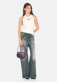 Top in maglia bianca a costine con dettaglio a taglio, abbinato a jeans a gamba larga blu sbiaditi e una piccola borsa viola. Scarpe nere con punta affusolata.
