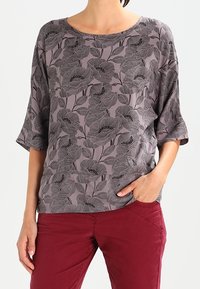 Blusa grigia con stampa floreale, dal taglio rilassato, scollo a barca e maniche a tre quarti, abbinata a pantaloni borgogna.