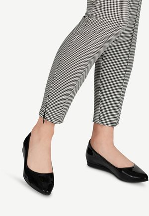Ballerines en cuir laqué noir avec un bout légèrement arrondi et un petit talon compensé, assorties à un pantalon à motif pied-de-poule.