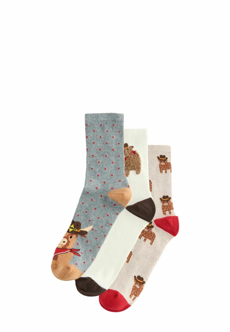 Trois paires de chaussettes : une grise avec des pois rouges, une blanche, et une brun clair décorée de motifs d'ours et de couleurs de bout contrastantes.