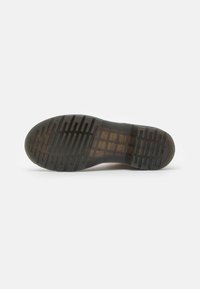 Suola di scarpa in gomma nera con superficie testurizzata, caratterizzata da profonde scanalature e punta arrotondata. Logo trasparente visibile nella zona del tallone.