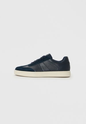 Mörkblå sneakers med en blandning av släta och texturerade material, en vit sula, platta snören och subtil detaljering på sidopanelerna.