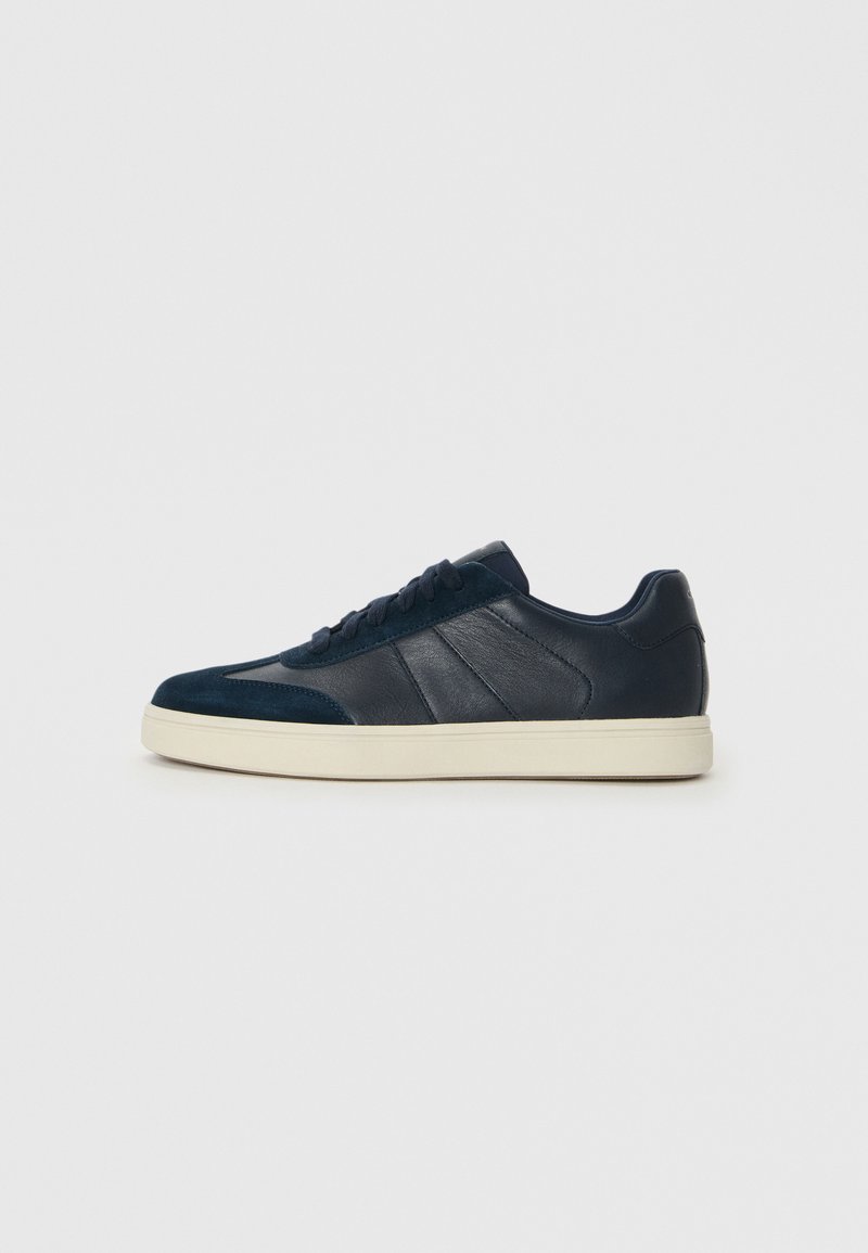 Navy blue sneakers featuring a mix of smooth and textured materials, with a white sole, flat laces, and subtle side panel detailing.
