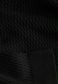 Detailní pohled na černou pletenou látku s různorodými texturovanými vzory a žebrovanými okraji na měkkém materiálu.