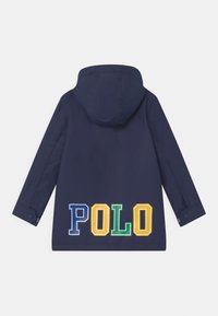 Námořnická kapucínová bunda s barevným nápisem "POLO" v modré, zelené, žluté a oranžové barvě. Vyrobeno z hladkého, povětrnostním podmínkám odolného materiálu.