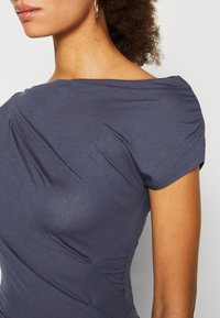 Navy blue short-sleeve top made from smooth fabric, featuring a draped design and subtle ruching along the sides.