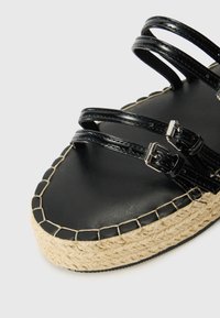 Sandalias de plataforma negras con tres correas estrechas, que cuentan con una suela de yute trenzado y un acabado suave y brillante en las correas.