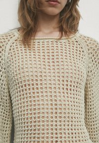 Strickpullover in hellbeige mit einem offenen Netzdesign, quadratischem Ausschnitt und langen Ärmeln. Weiche Textur mit lockerer Passform.